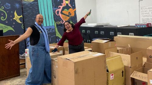 Sukari and Lupe stand in a warehouse full of boxes of instruments