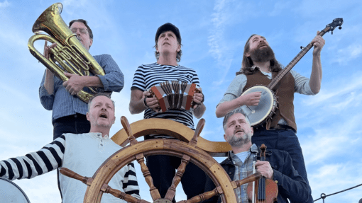 John Kraus and the Goers playing music on a boat in front of the ship's wheel