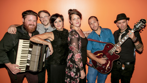Bon Bon Vivant band smiling with instruments posing against an orange wall