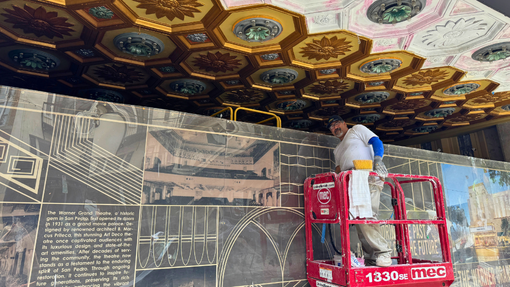 A man poses while working on restoring the lights in the entrance to the Warner Grand Theatre